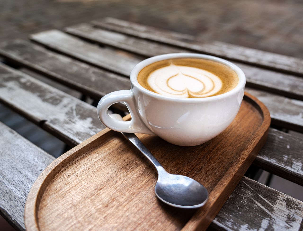 A cup of cappuccino with heart-shaped latte art on a wooden table, perfect for a coffee break outdoors.