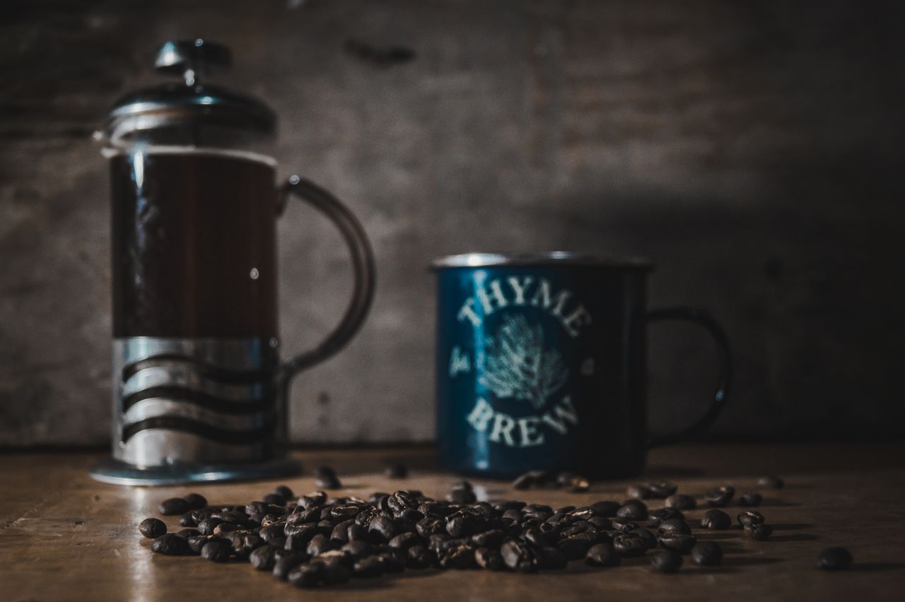 A cozy scene featuring a French press, a mug labeled 'Thyme for Brew', and coffee beans on a wooden table.